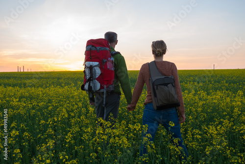 Couple of travelers with backpacks stand in a field of yellow flowers