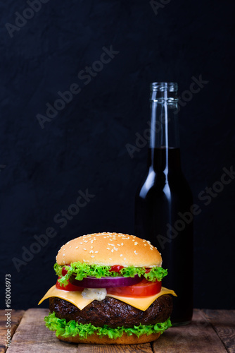 Burger and drink in glass bottle on dark background