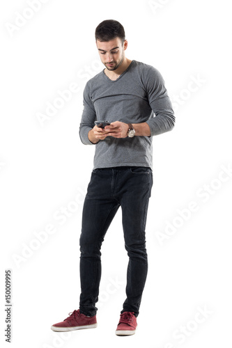 Stylish young trendy man typing message on cellphone. Full body length portrait isolated on white studio background.  © sharplaninac