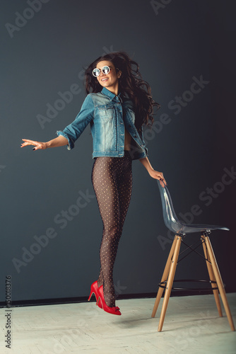 gorgeous girl with red lipstick and white sunglasses dressed in a blue  jacket red high heel shoes and transparent tights without panties Stock  Photo