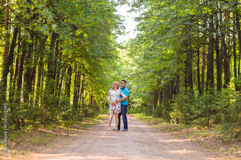 happy young pregnant woman with her husband walking in a park