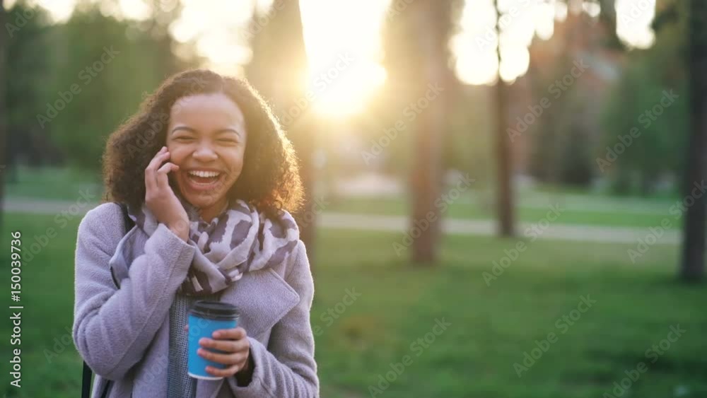 Attractive mixed race girl talking smartphone and drinking coffee in city park with bags. Young woman after shopping on mall sale