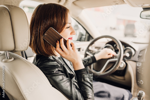 Beautiful business woman is talking on the mobile phone and smiling while sitting in the car