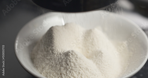 Handheld shot of sieving flour with mug sieve on plate closeup, 4k photo
