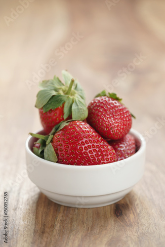 ripe organic strawberries in white bowl on wood table  with copy space