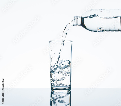 Pouring drinking water from bottle into drinking glass on white background