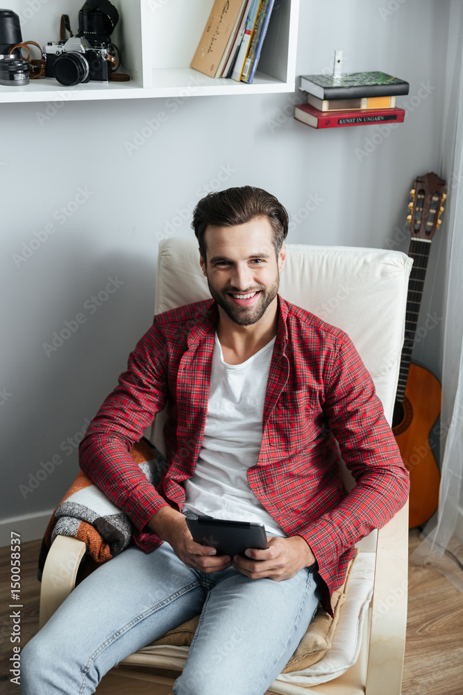 Happy young bearded man using tablet computer.