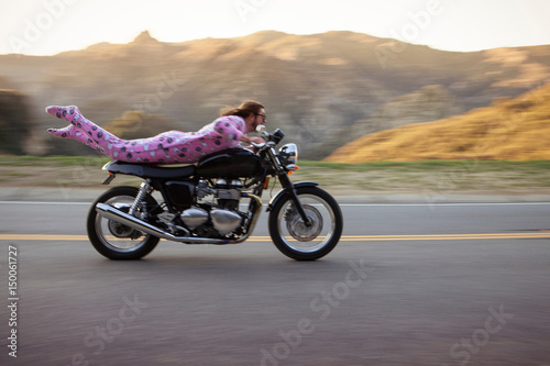 Man wearing onesie lying on front riding motorcycle, Malibu Canyon, California, USA photo