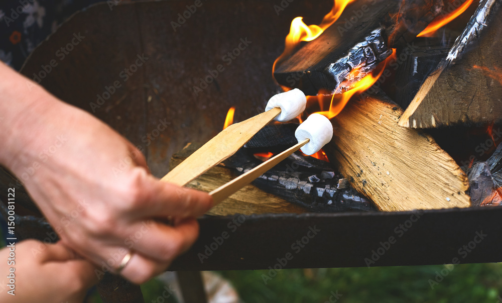 Fototapeta premium flame grilled and wood burning in fire and hands with Sticks with marshmallows on fire close up. family BBQ party in outdoor or home garden.