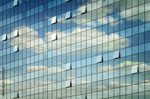 Modern glass office building with clouds and sky reflections