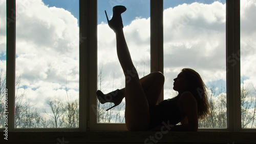 Silhouette of girl on high hilts in front of window. © Demian