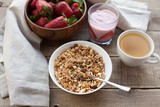 A bowl of homemade granola with yogurt and fresh strawberries on a wooden background. Healthy breakfast with green tea