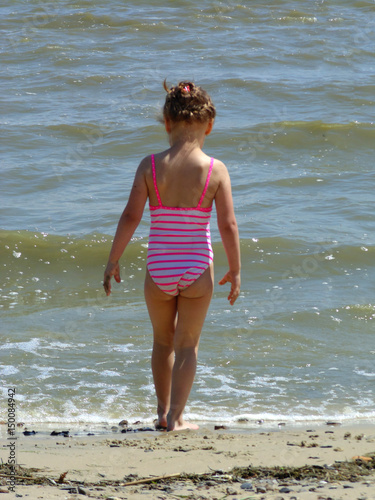Canvas Print The baby in a swimsuit is standing by the water