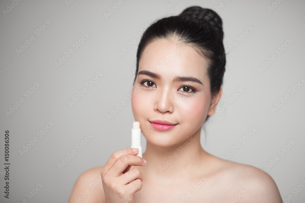 Asian woman applying hygienic lip balm over grey background Asian woman applying hygienic lip balm over grey background