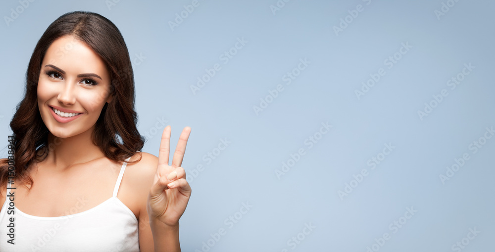 Woman showing two fingers or victory gesture, on grey Woman showing two fingers or victory gesture, on grey