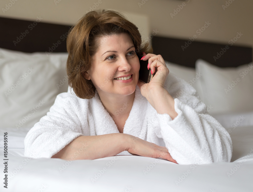 Woman in bathrobe talking on phone in hotel room Woman in bathrobe talking on phone in hotel room