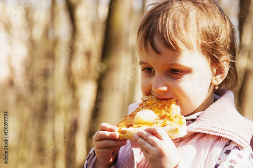 Little girl enjoying a delicious pizza in nature (food, hunger, pleasure)