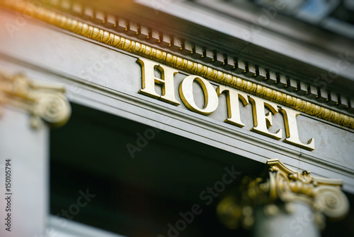 Canvas Print Sun flare above hotel word with golden letters on luxury hotel with beautiful co