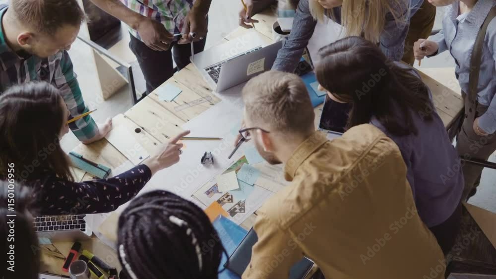 Top view of young team working on new project. Group of mixed race people standing near the table and discussing.