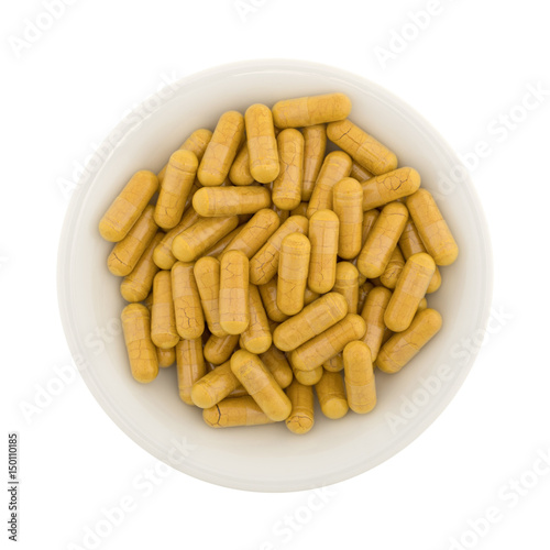 Top view of turmeric capsules in a small bowl isolated on a white background.