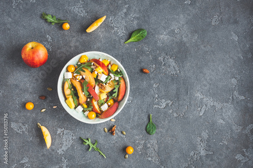 Peach salad. Spinach leaves, arugula, sliced peaches, mango, nuts, feta cheese on black background. Fruit salad. Flat lay, top view, copy space