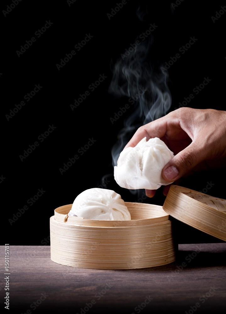 The man's hand is holding a hot steamed bun in a bamboo steamer, chinese dim sum