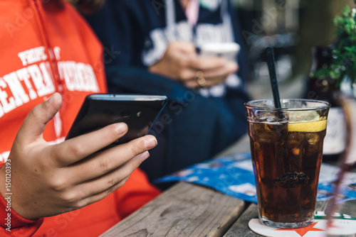 Refreshing glass of cola on wooden table in a bar while young is connected with phone