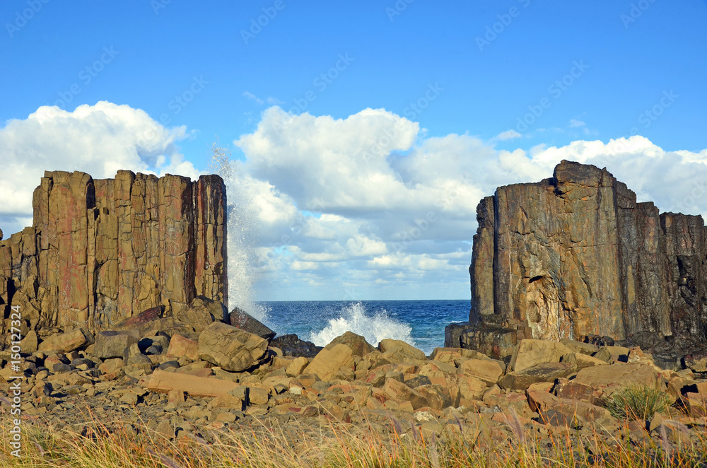 Waves breaking in the gap between basalt rock formations with a view to the sea at Bombo Headland quarry, New South Wales coast, Australia