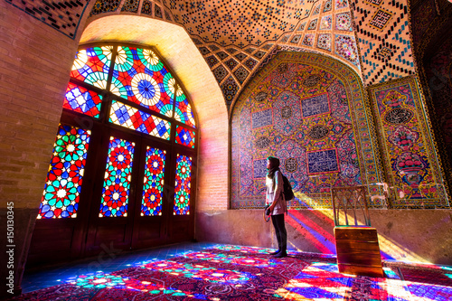An asian female tourist facing the multicolors light through spectacular stained glass in Nasir Al-Mulk Mosque (Pink Mosque) in Shiraz - Iran. photo