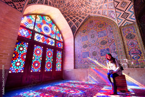 An asian female tourist facing the multicolors light through spectacular stained glass in Nasir Al-Mulk Mosque (Pink Mosque) in Shiraz - Iran. photo