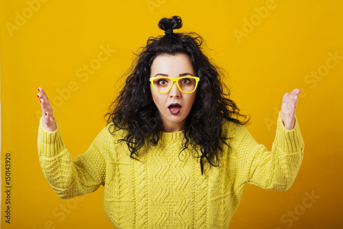 Surprised young woman in glasses with modern hairstyle over yellow background.