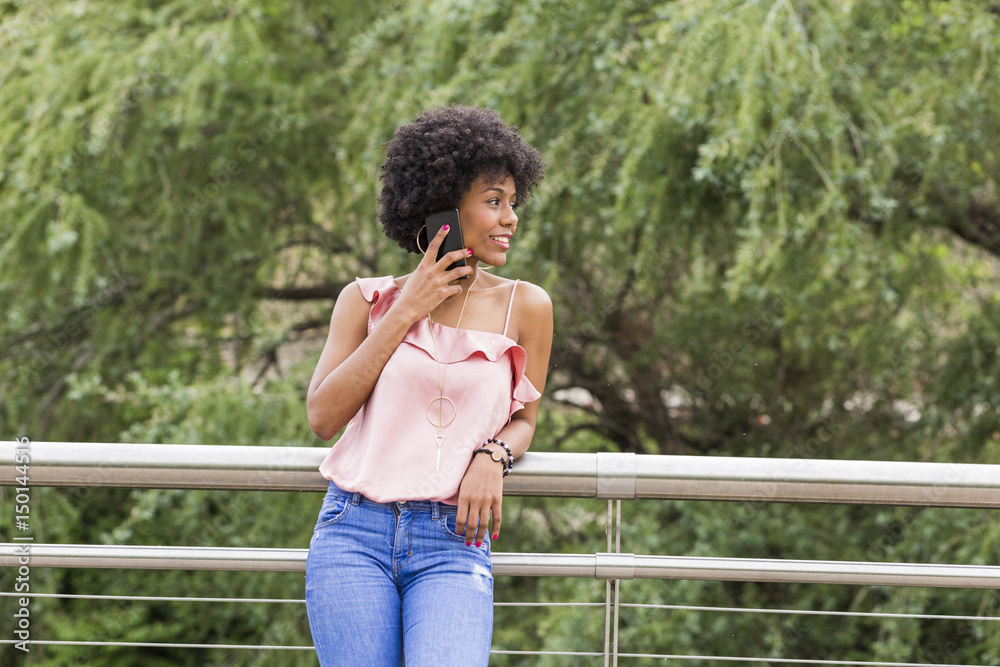 portrait of  a Happy young beautiful afro american woman smiling and talking on her mobile phone. Green background. Spring or summer season. Casual