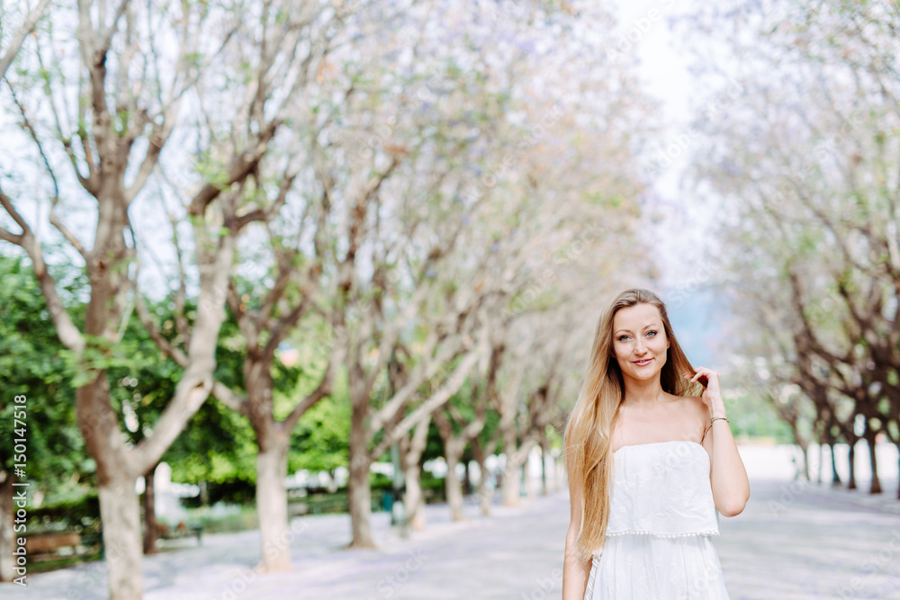 Blonde woman in blossom tree alley white dress summer feeling Blonde woman in blossom tree alley white dress summer feeling