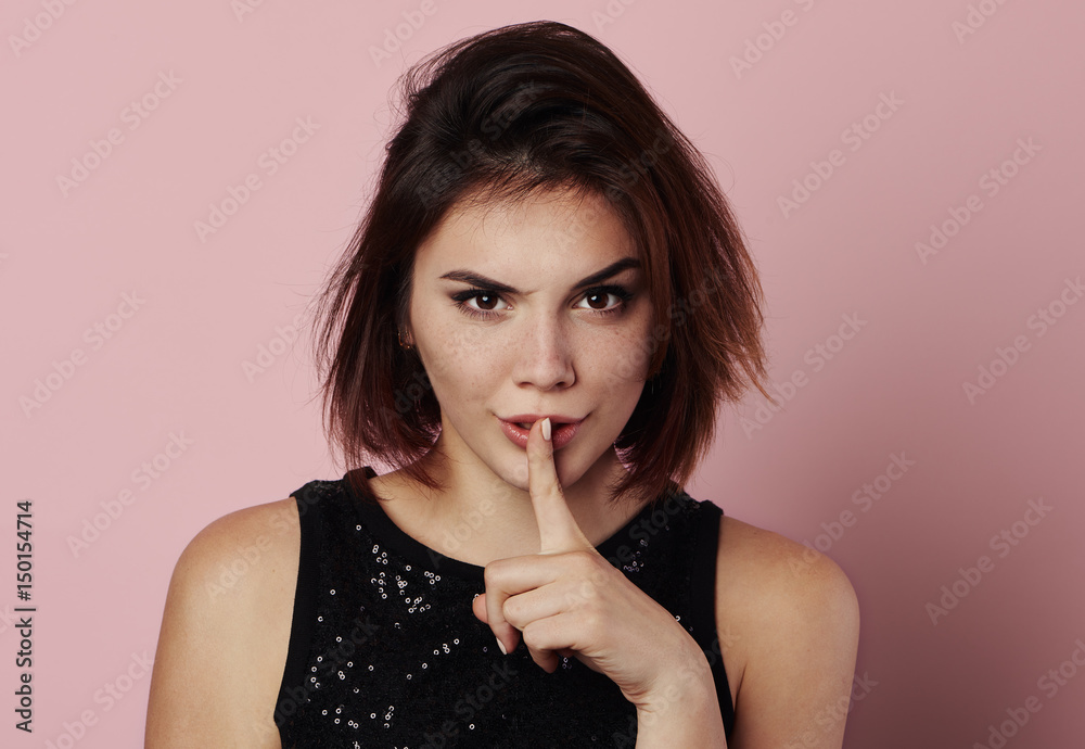 Fototapeta premium Young fashionable lady showing hush gesture, posing in studio. 