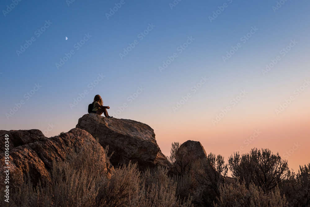 Sunset at the top of Antelope Island with silhouette of female sitting on rocks near Salt Lake City, Utah with moon