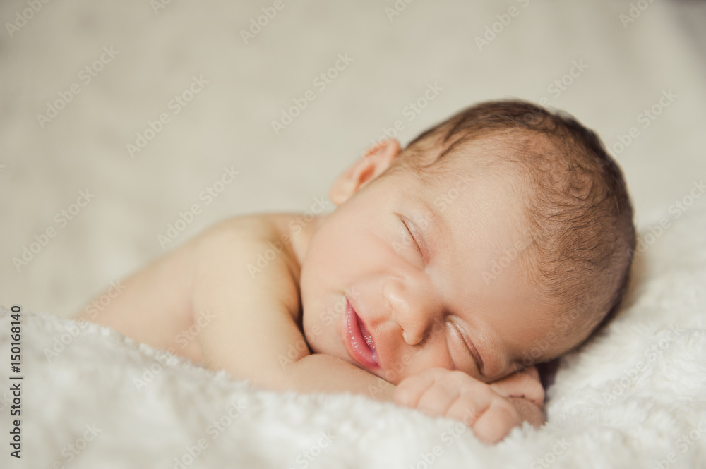 Portrait close up studio Shot of Eight day old Smiling newborn baby is sleeping on his stomach on white wool blanket. Portrait close up studio Shot of Eight day old Smiling newborn baby is sleeping on his stomach on white wool blanket.