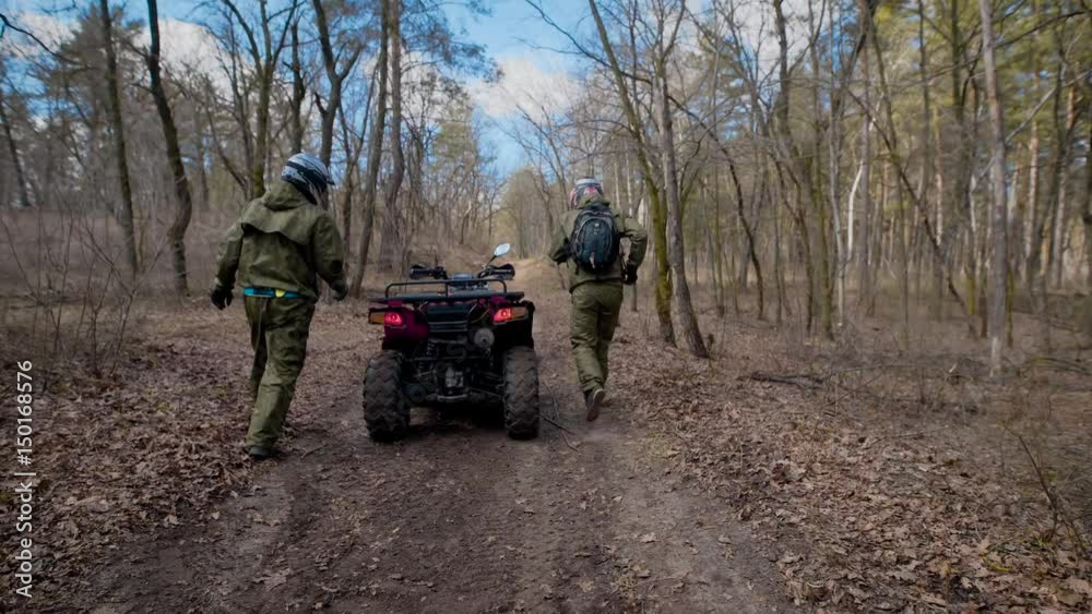 Two athletes who wear protective helmets and clothes jump on the ATV and swiftly ride along the autumn forest Two athletes who wear protective helmets and clothes jump on the ATV and swiftly ride along the autumn forest
