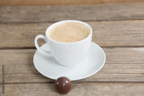 Coffee cup and chocolate ball on wooden surface