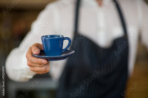 Mid-section of waiter offering a cup of coffee