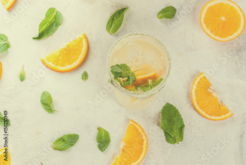 Summer drink. Fresh orange and mint lemonade with ice in glasses, light grey stone marble table, selective focus, toned top view