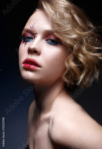 A young girl with a short haircut and bright creative makeup. A beautiful model with sparkles on the face and red lips. Evening makeup, beauty of the face. Photo is taken in a studio.