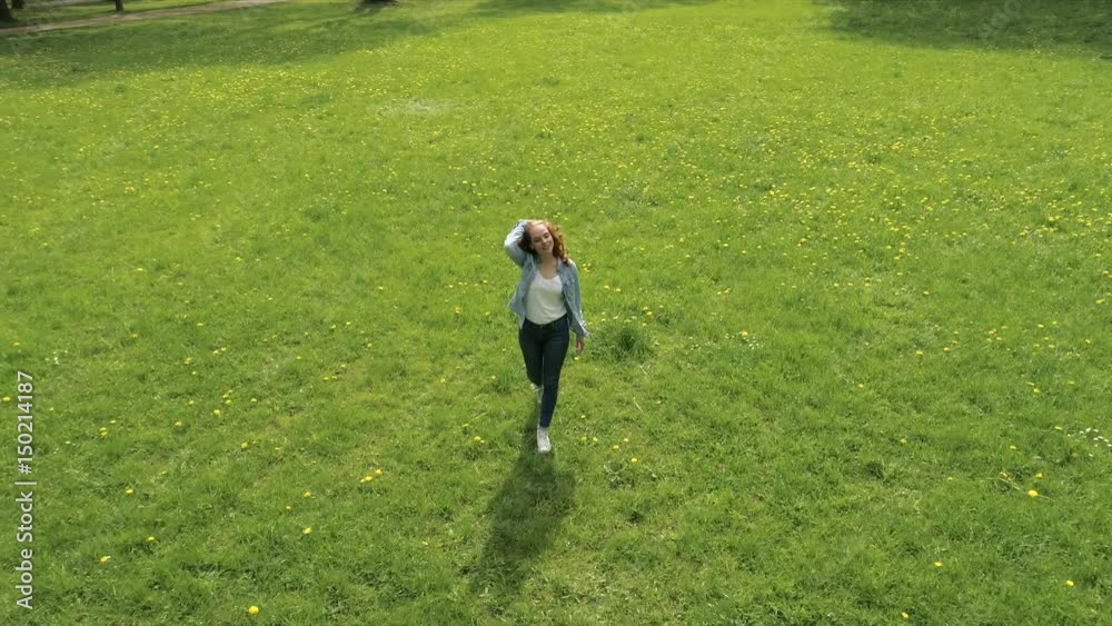 lachende frau geht über eine grüne wiese und streckt die arme nach oben