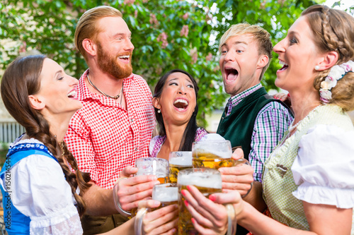 Fünf Freunde, Männer und Frauen, haben Spass in Biergarten beim Anstoßen mit Maßkrügen