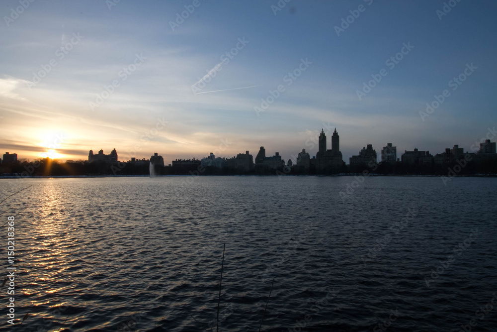 Sunset reflects on lake and silhouette buildings with blue sky