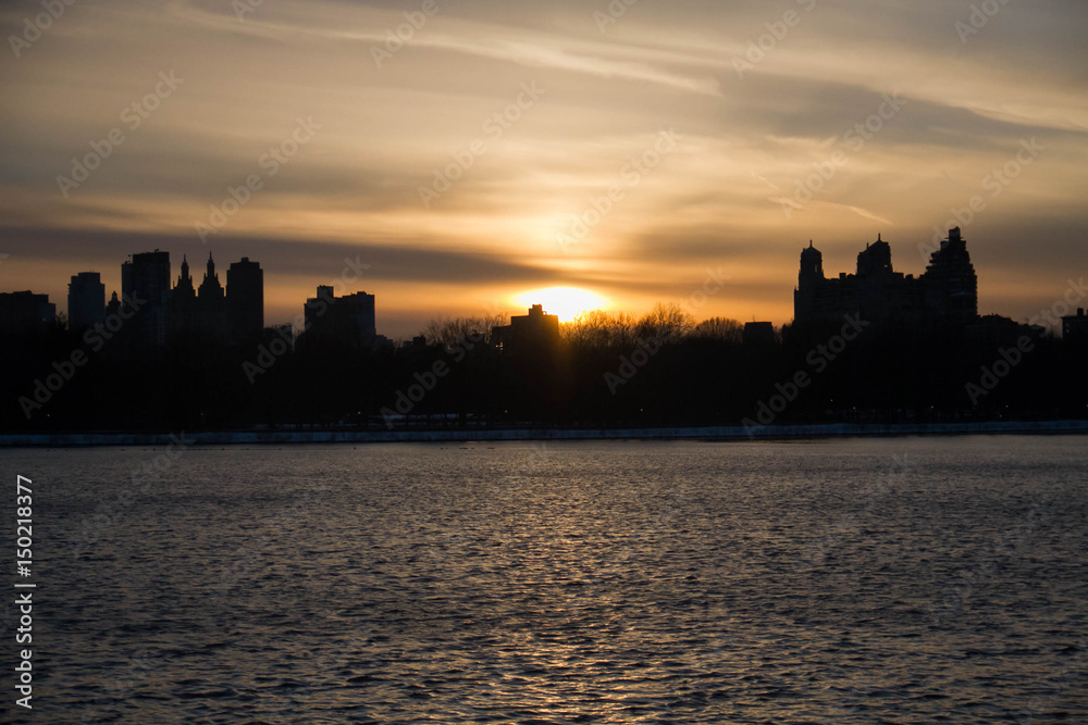 Sunset and silhouette buildings over lake, New York