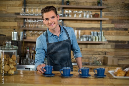 Smiling waiter preparing cup of coffee at counter