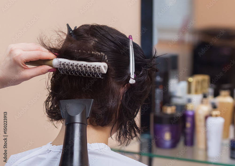 Fototapeta premium The hairdresser dries her hair a brunette girl in a beauty salon.