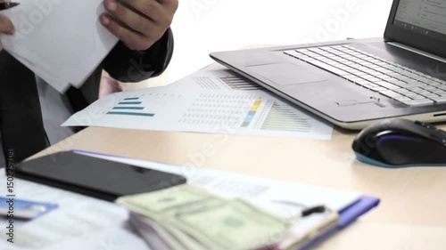 The businessman is working at the desk, examining reports and counting money.
