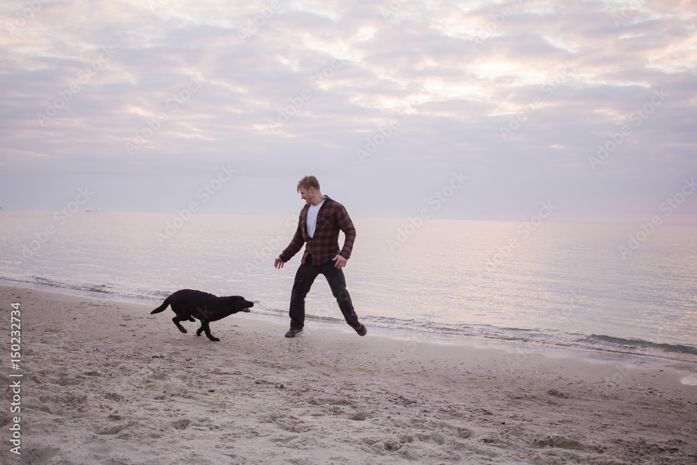 young man run and playing with black dog on the beach