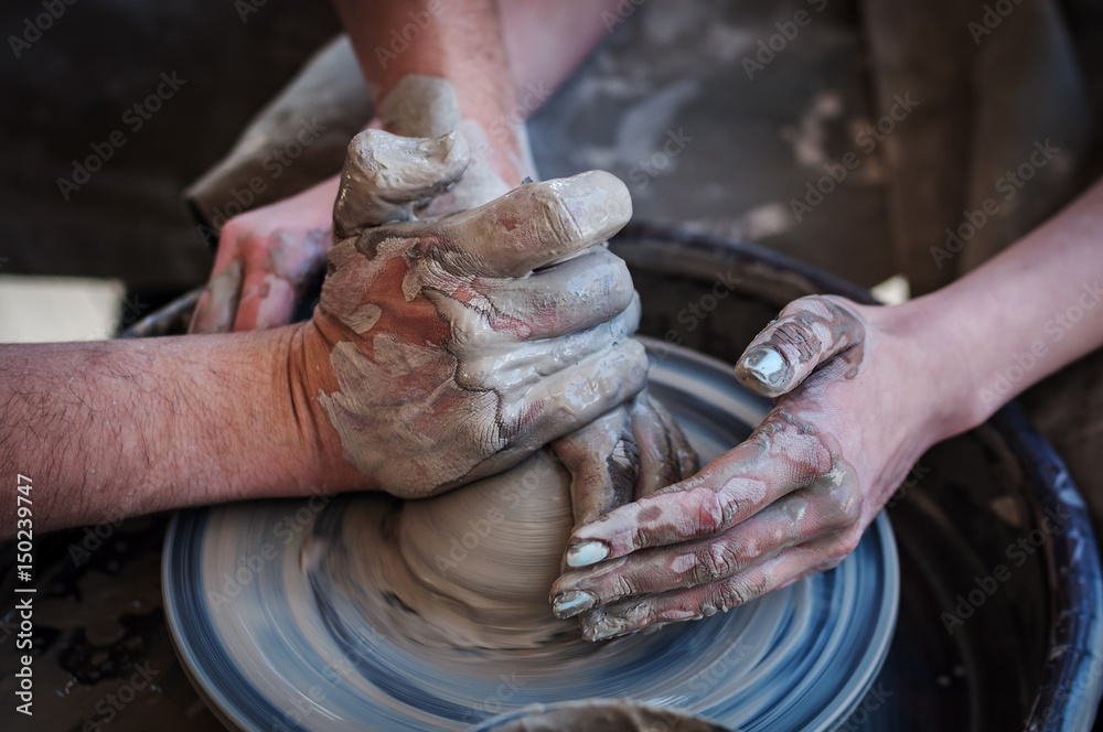 Naklejka premium Woman and man hands. Potter at work. Creating dishes. Potter's wheel. Dirty hands in the clay and the potter's wheel with the product.